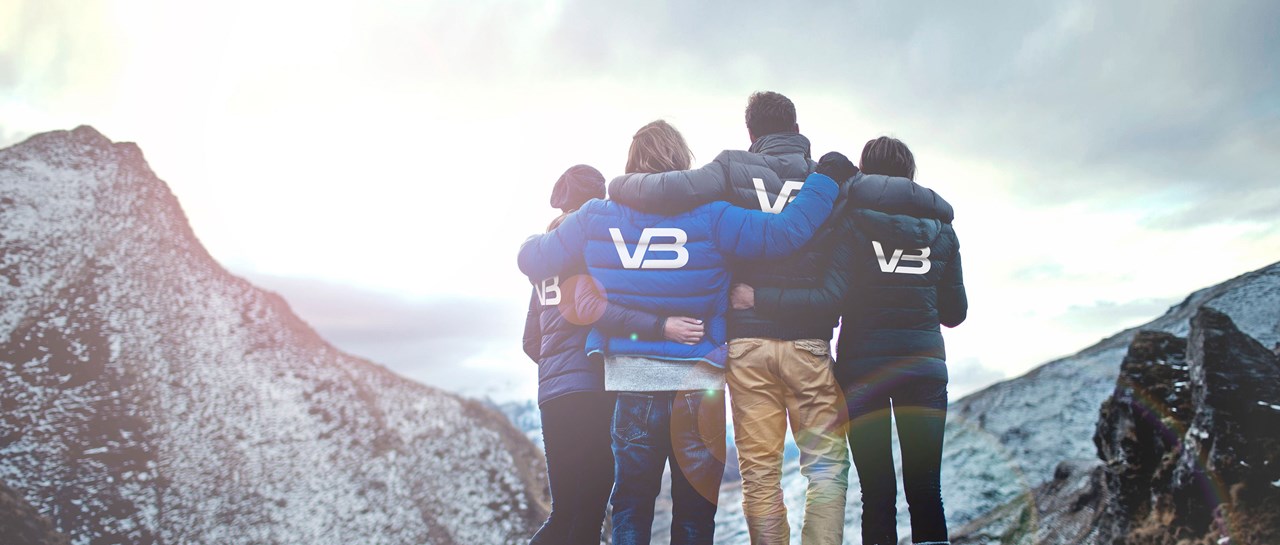 VB Rørleggere ser ut mot et fjell med logo på baksiden av jakkene sine